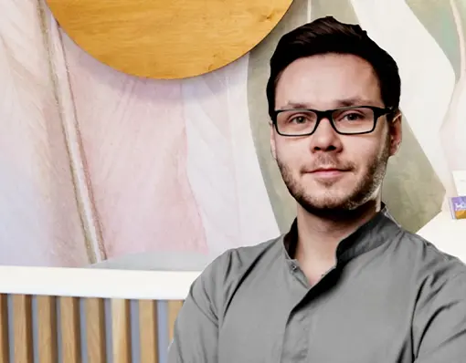 Portret lekarza stomatologa w okularach i szarym fartuchu medycznym, w tle widoczny fragment recepcji.