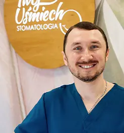 Uśmiechnięty lekarz stomatolog w ciemnoniebieskim fartuchu medycznym na tle logo „Twój Uśmiech Stomatologia”.