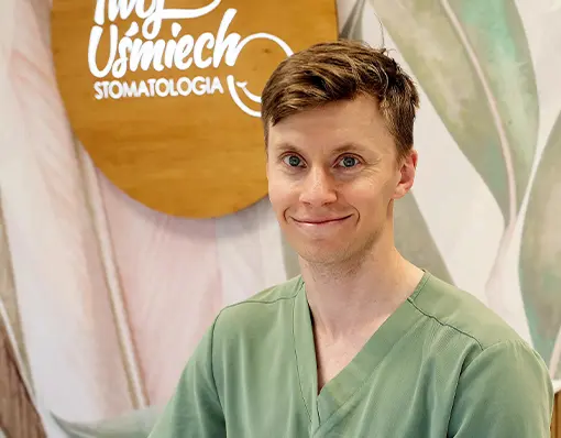Portret lekarza stomatologa w zielonym fartuchu medycznym, uśmiechającego się na tle logo „Twój Uśmiech Stomatologia”.