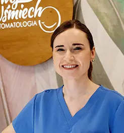 Uśmiechnięta lekarka stomatolog w niebieskim fartuchu medycznym na tle logo „Twój Uśmiech Stomatologia”.