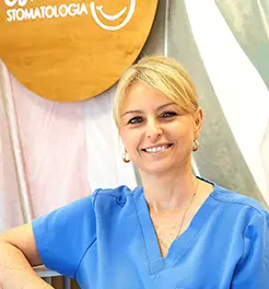 Uśmiechnięta lekarka stomatolog w niebieskim fartuchu medycznym na tle logo kliniki dentystycznej.