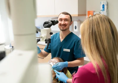Dentysta leczący pacjentkę przy użyciu mikroskopu stomatologicznego w asyście higienistki.