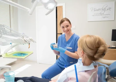 Uśmiechnięta dentystka pokazująca pacjentce model uzębienia w gabinecie stomatologicznym.