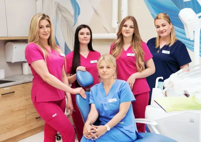 Personel medyczny w gabinecie stomatologicznym wokół fotela dentystycznego.