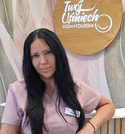 Portret uśmiechniętej kobiety w różowym fartuchu medycznym, na tle logo gabinetu stomatologicznego.