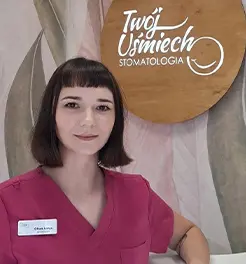 Portret lekarki stomatolog w niebieskim fartuchu medycznym z identyfikatorem, na tle logo „Twój Uśmiech Stomatologia”.